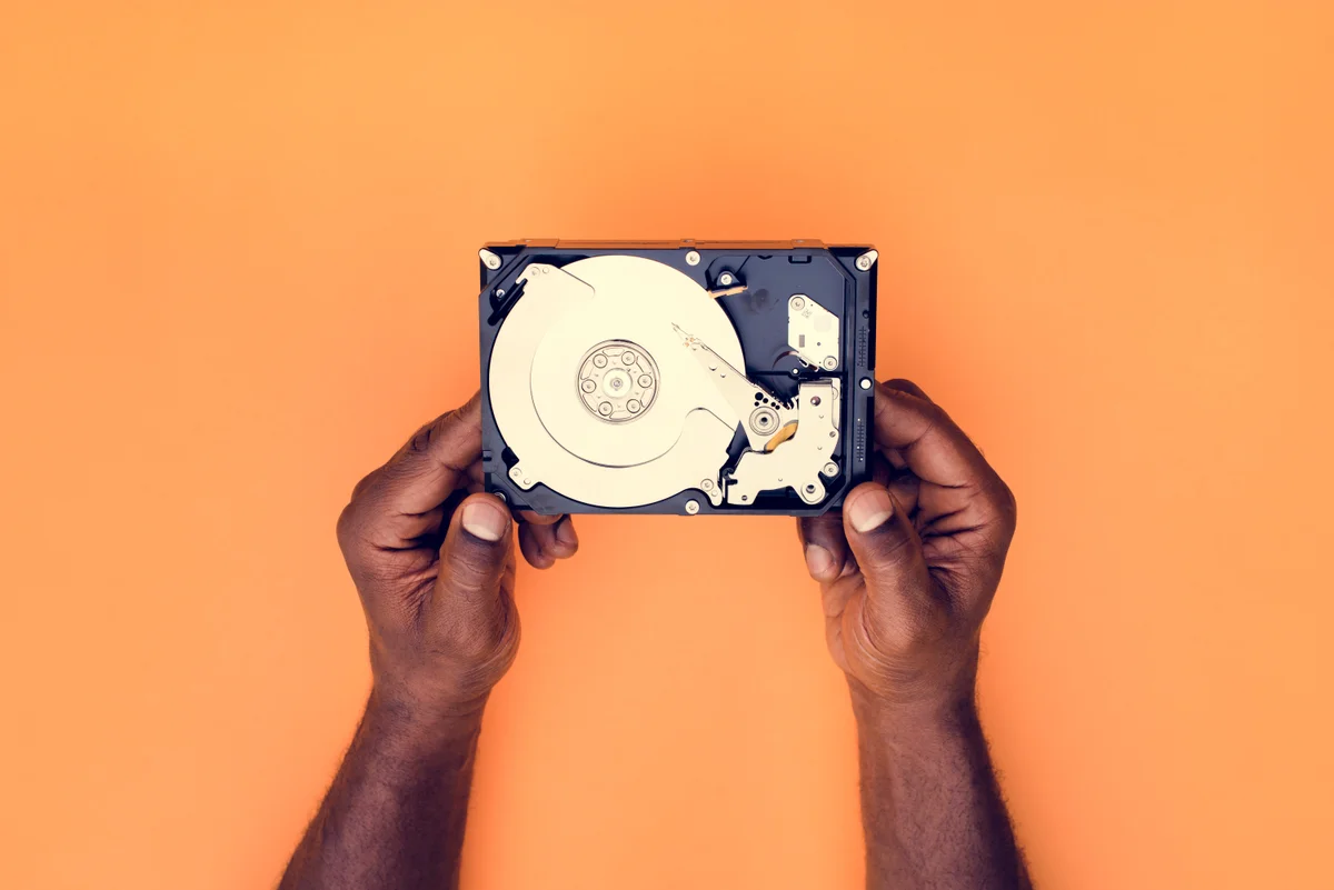 Mains tenant un disque dur ouvert sur fond orange, illustrant la sauvegarde et la restauration AD